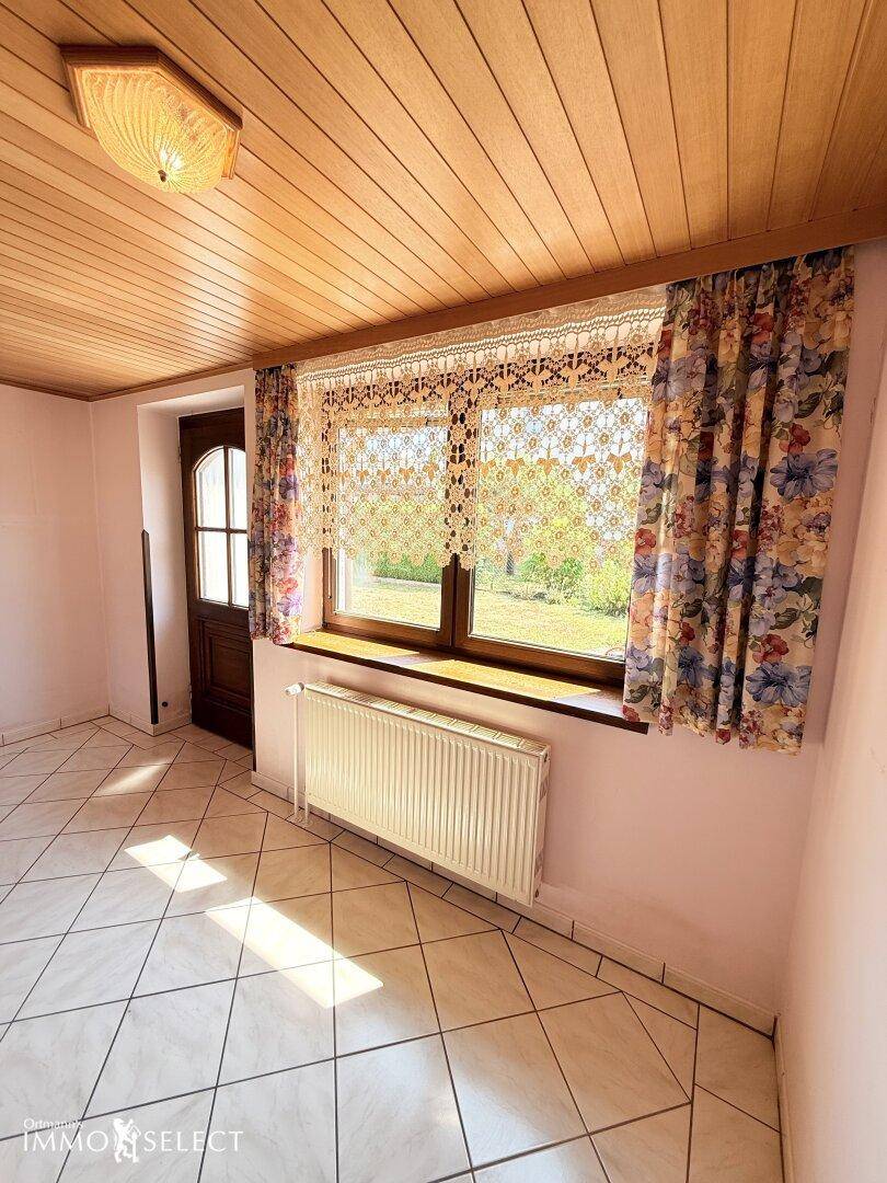 Heller Flur mit Fliesenboden und Holzdecke, ein Fenster bietet einen grünen Ausblick.