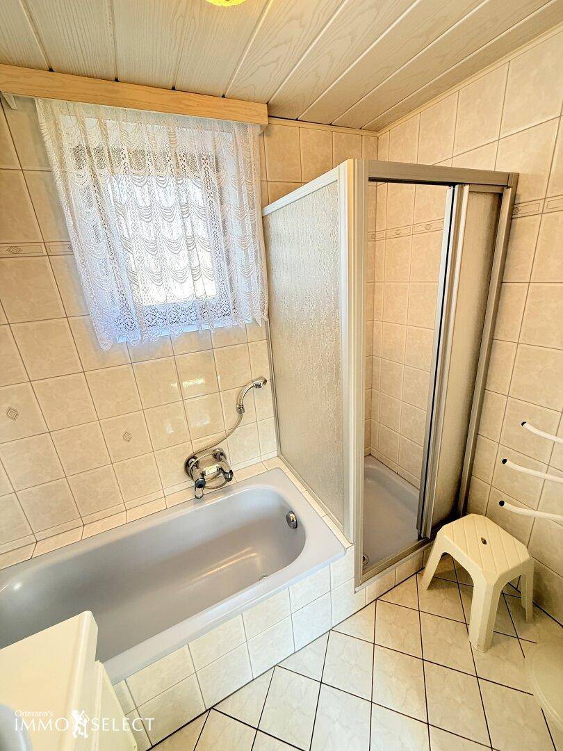 Badezimmer mit Badewanne, separater Duschkabine und hellen Fliesen an Wänden und Boden.