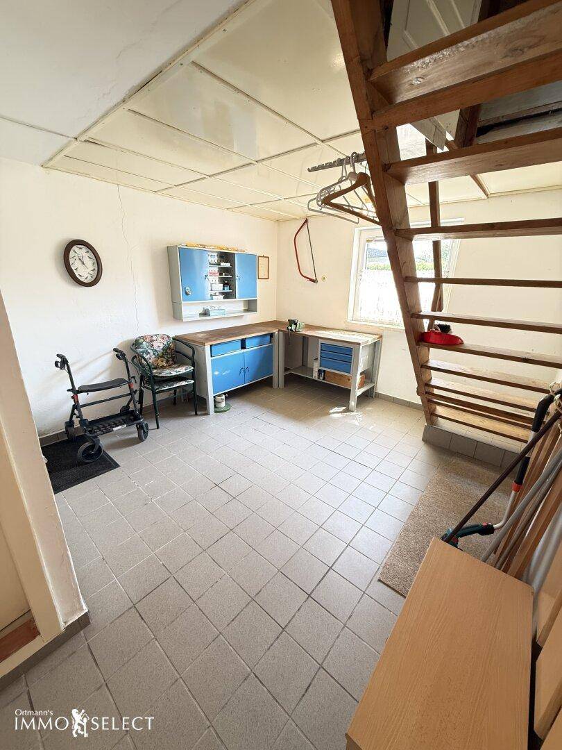 Werkstattbereich mit Fliesenboden, Werkbank und einer Holztreppe, ideal für Heimwerker.