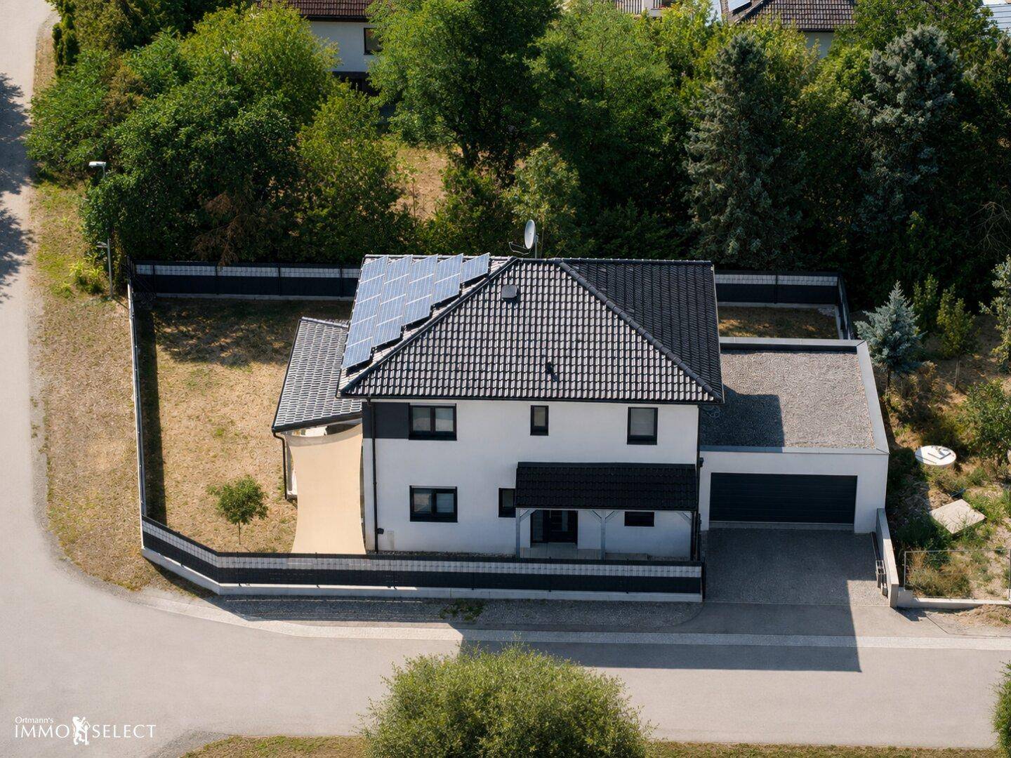 Luftaufnahme eines modernen Einfamilienhauses mit Solaranlage auf dem Dach und umzäuntem Grundstück.