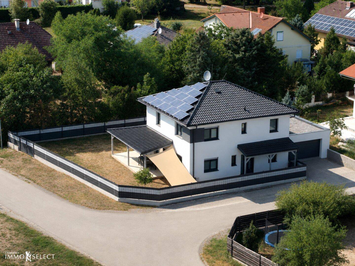 Luftaufnahme eines modernen Einfamilienhauses mit Solaranlage auf dem Dach und umzäuntem Grundstück.