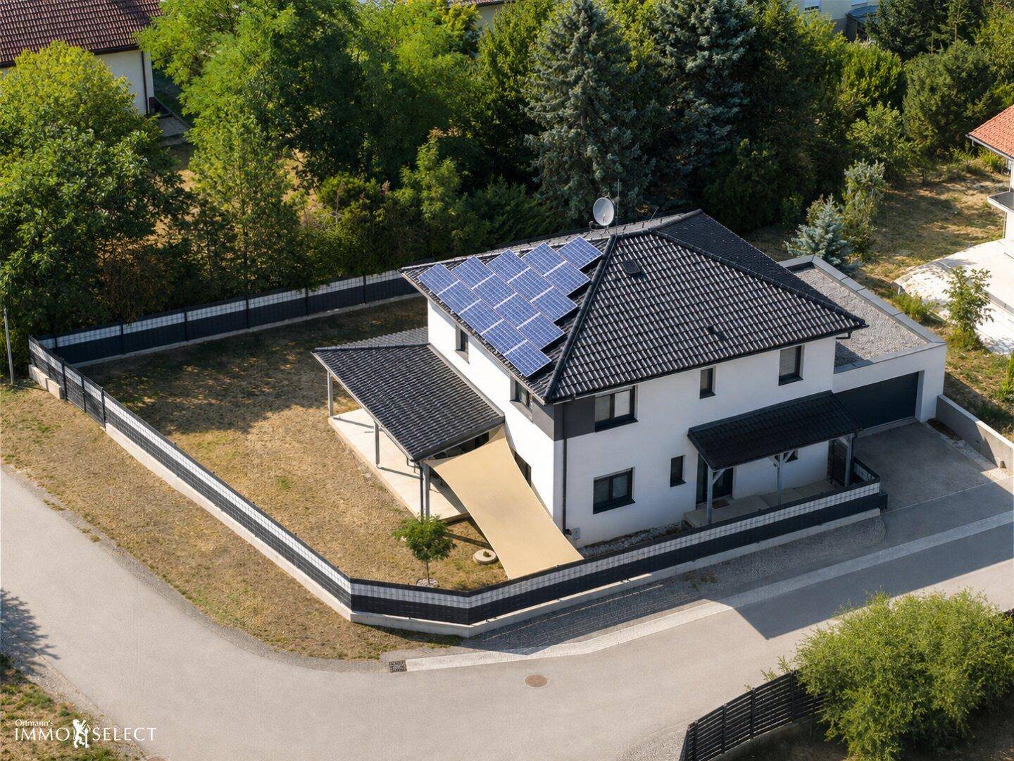 Luftaufnahme eines modernen Einfamilienhauses mit Solaranlage auf dem Dach und umzäuntem Grundstück.