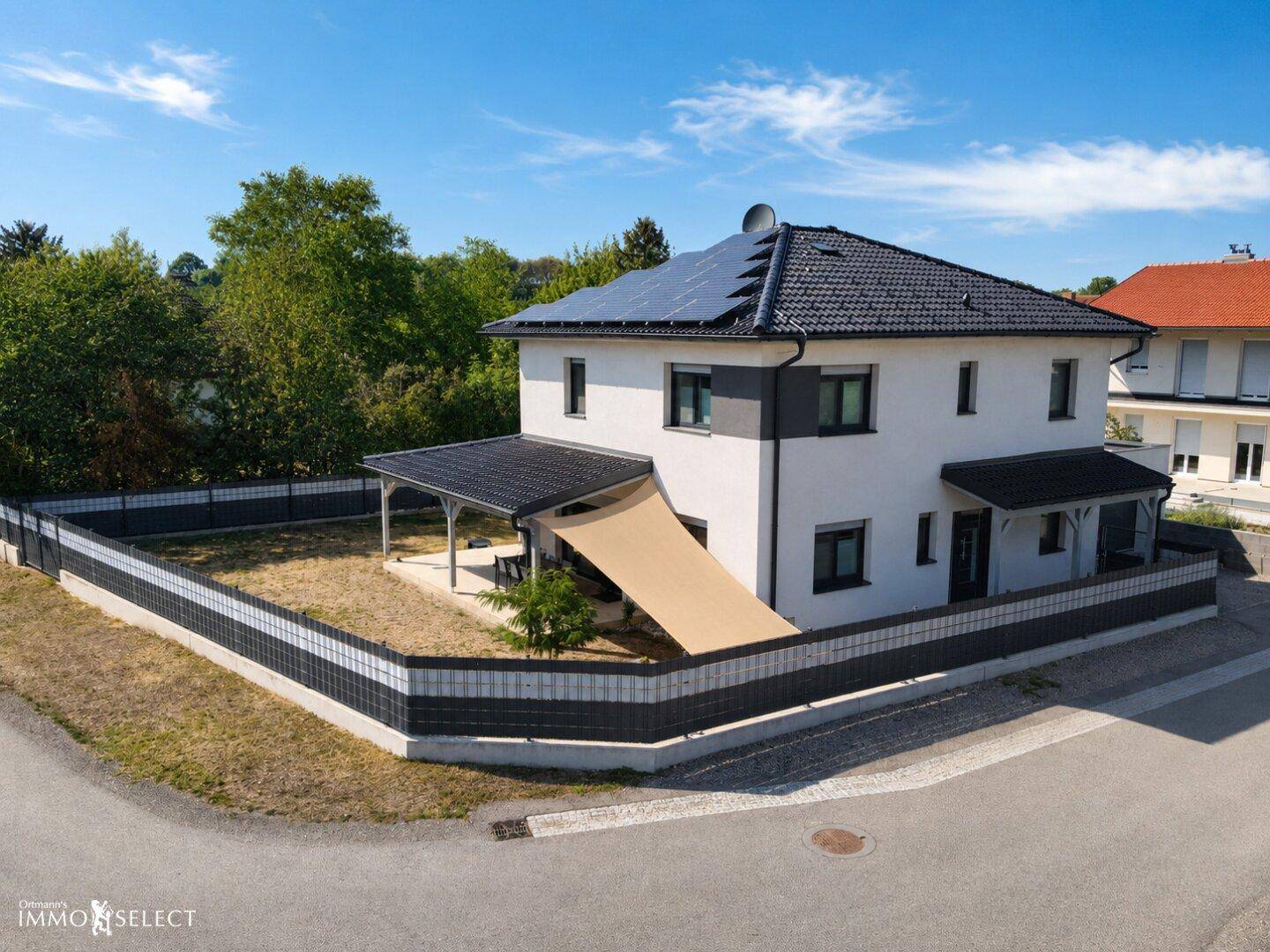 Luftaufnahme eines modernen Einfamilienhauses mit Solaranlage auf dem Dach und umzäuntem Grundstück.