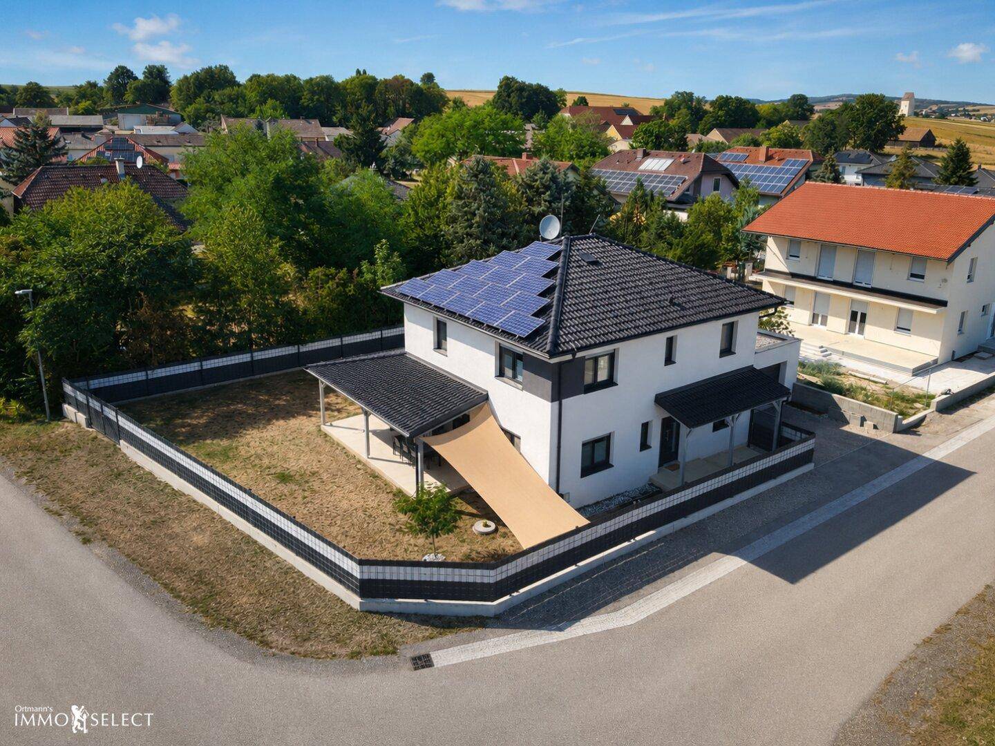 Luftaufnahme eines modernen Einfamilienhauses mit Solaranlage auf dem Dach und umzäuntem Grundstück.