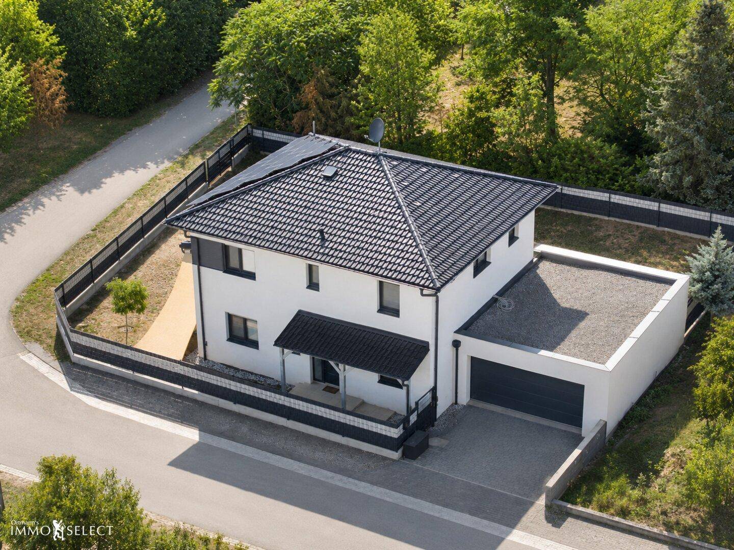 Luftaufnahme eines modernen Einfamilienhauses mit dunklem Dach, Solaranlage und Garage.