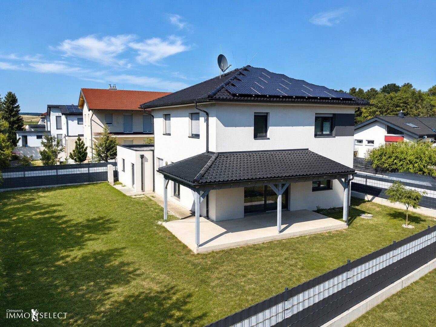 Rückansicht des Hauses mit großem, gepflegtem Rasen und einer überdachten Terrasse.