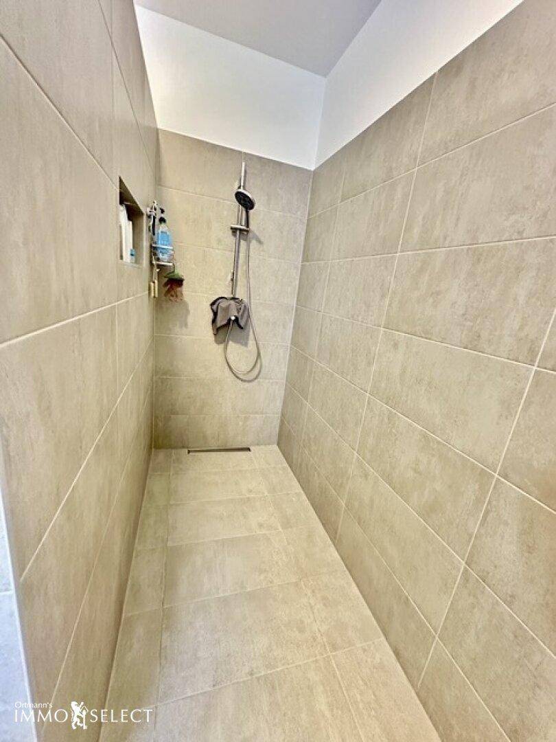 Ebenerdige Dusche mit modernen grauen Fliesen und Duscharmatur.