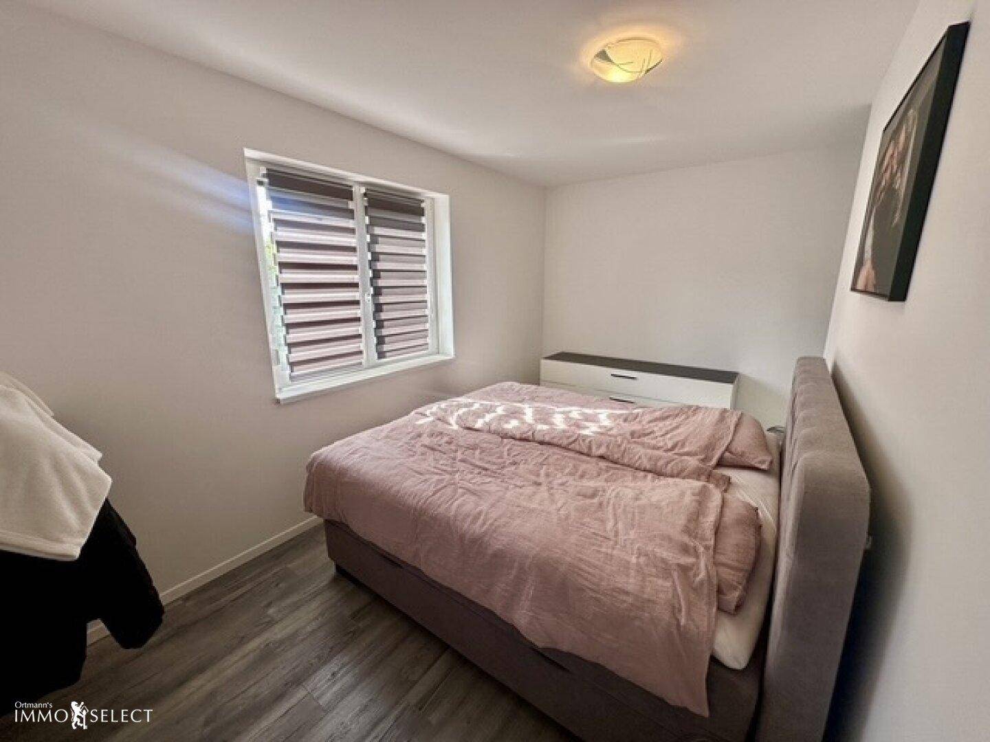 Gemütliches Schlafzimmer mit Doppelbett, modernem Laminatboden und Fenster mit Jalousien.