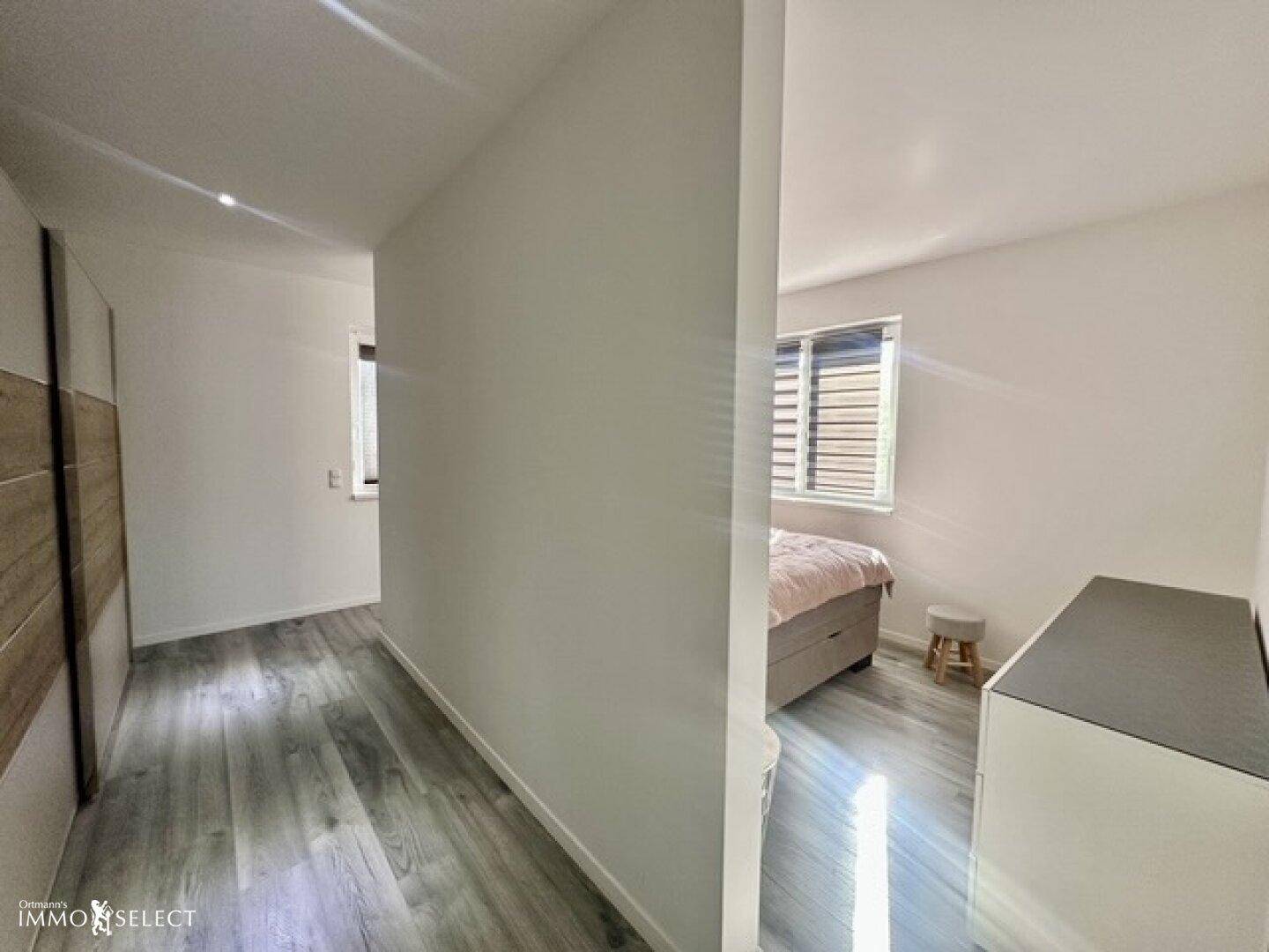 Heller Flur mit modernem Laminatboden und Einbauschrank, der zu einem Schlafzimmer führt.