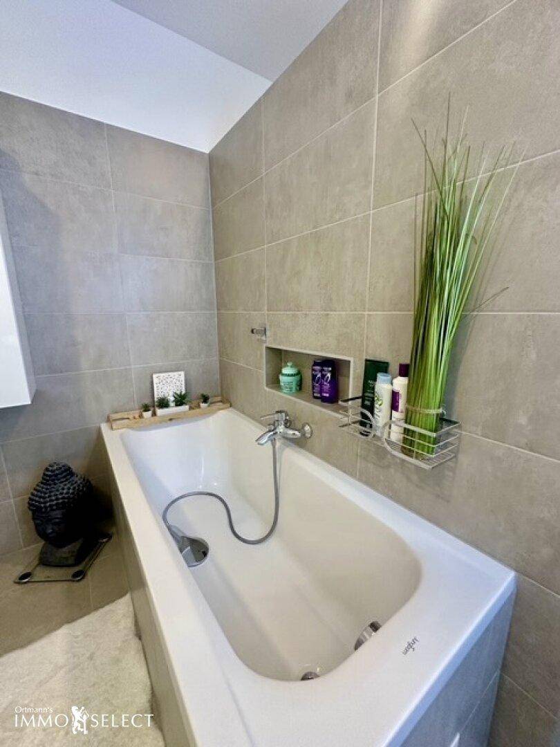 Detailansicht der Badewanne in einem modernen Badezimmer mit hellgrauen Fliesen und Dekoration.