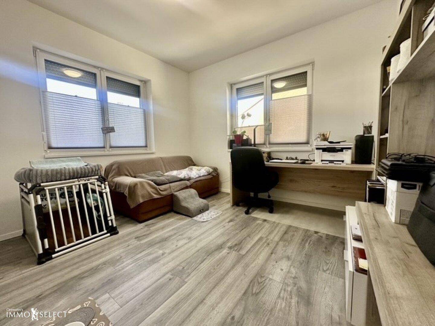 Helles Arbeitszimmer mit Laminatboden, Schreibtisch und einem Schlafsofa.