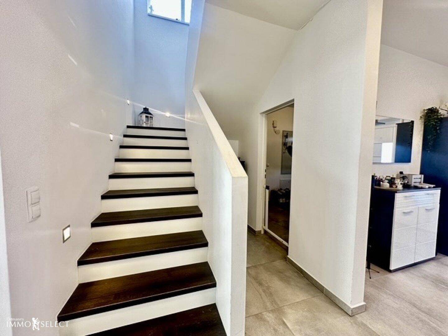 Heller Eingangsbereich mit moderner Treppe und Blick auf die Garderobe.