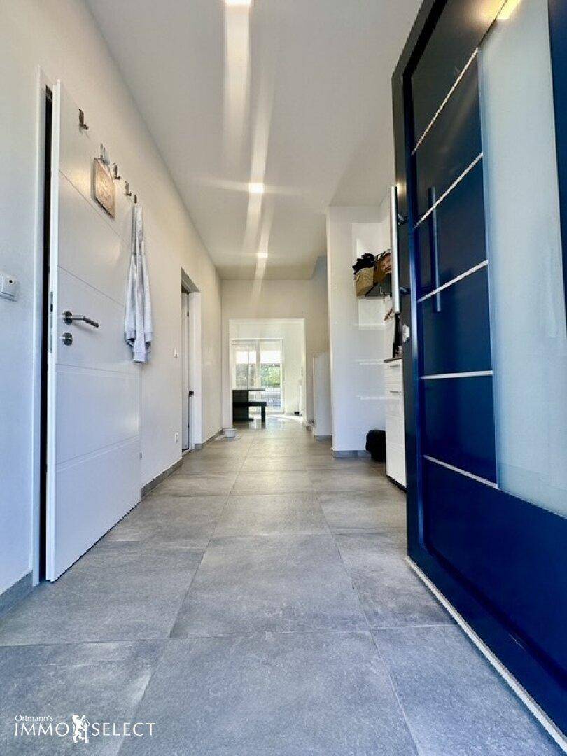 Heller Eingangsbereich mit grauen Fliesen, Garderobe und einer modernen blauen Haustür.