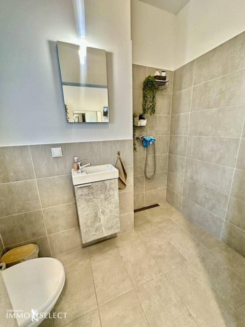 Modernes Badezimmer mit Toilette, kleinem Waschbecken und einer ebenerdigen Dusche.