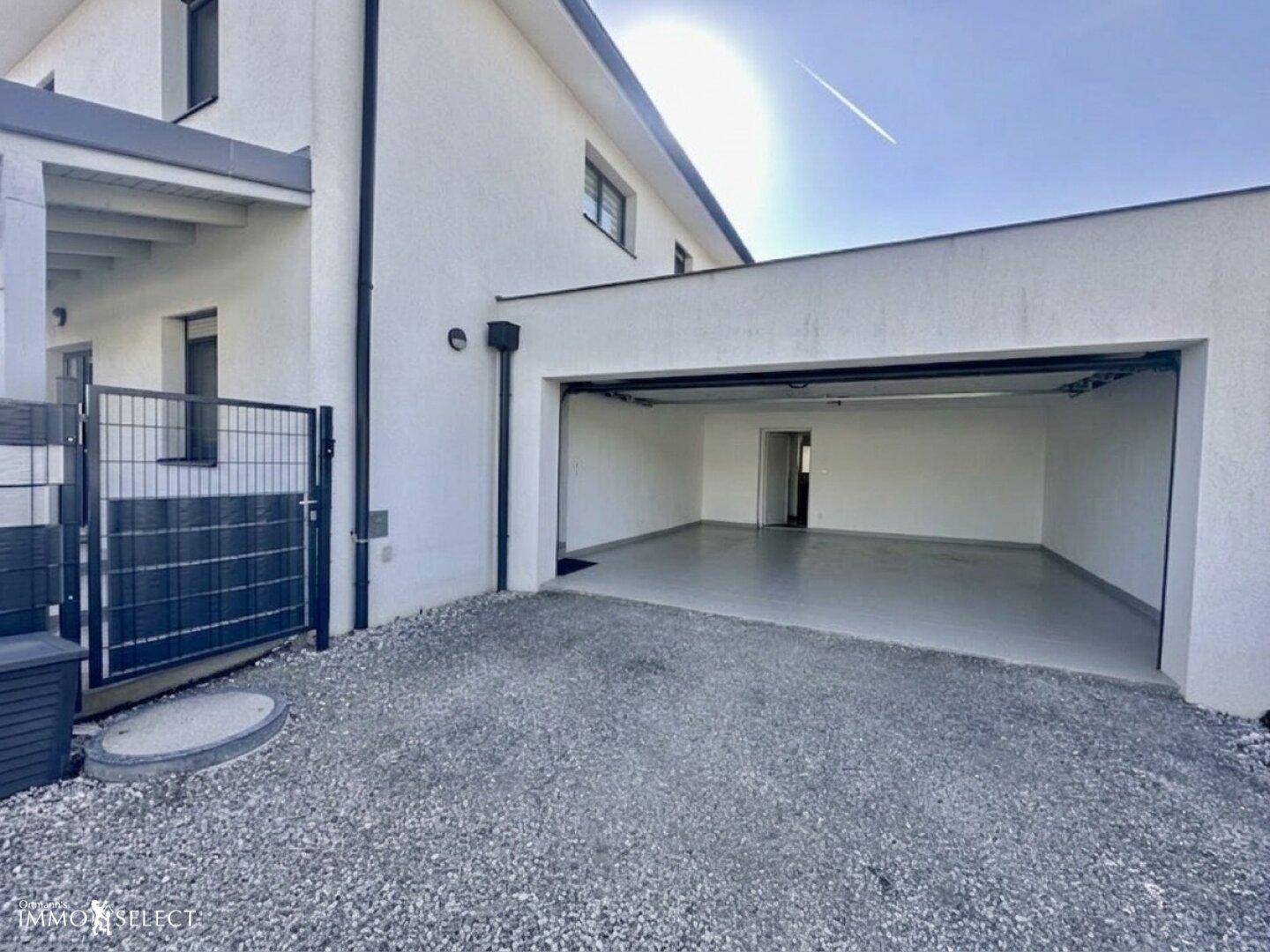 Außenansicht des Hauses mit offener Garage und Kiesauffahrt, bietet ausreichend Parkmöglichkeiten.