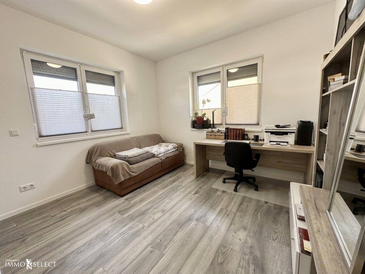 Helles Arbeitszimmer mit Schreibtisch, Sofa und zwei Fenstern, ausgestattet mit Laminatboden.