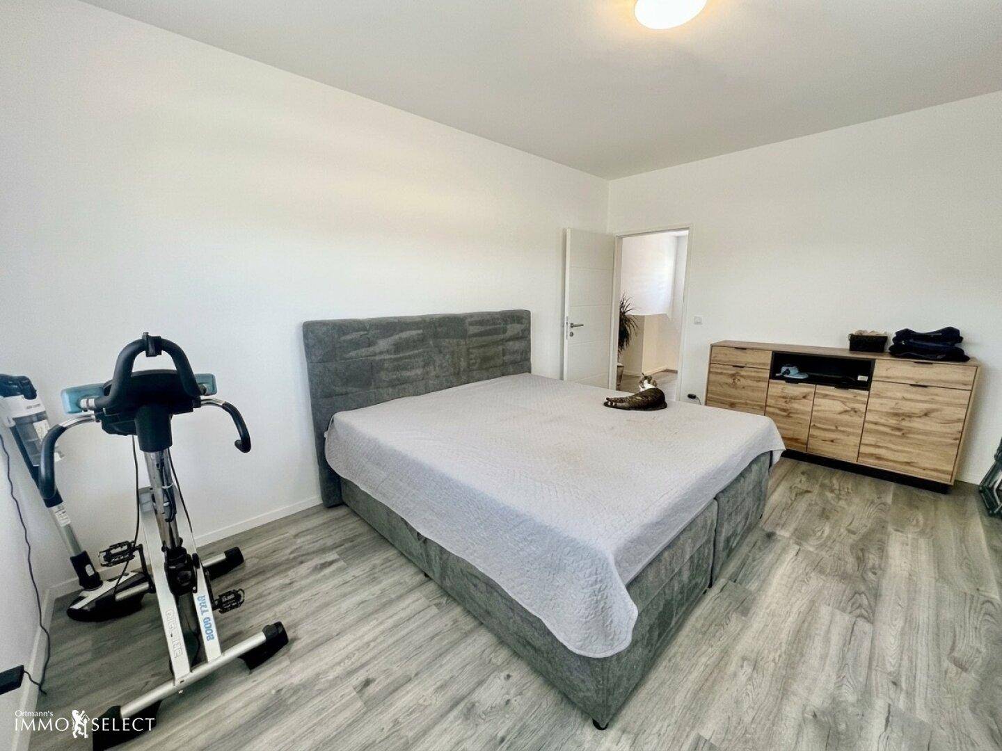 Geräumiges Schlafzimmer mit großem Bett, Holzkleiderschrank und einem Fitnessgerät.