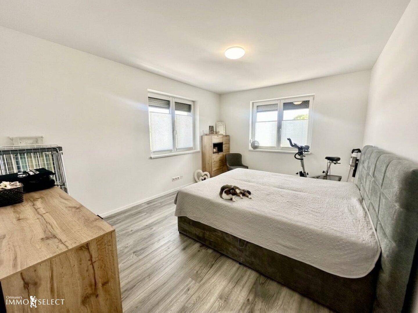 Helles Schlafzimmer mit großem Bett, zwei Fenstern und einem Holzschrank.
