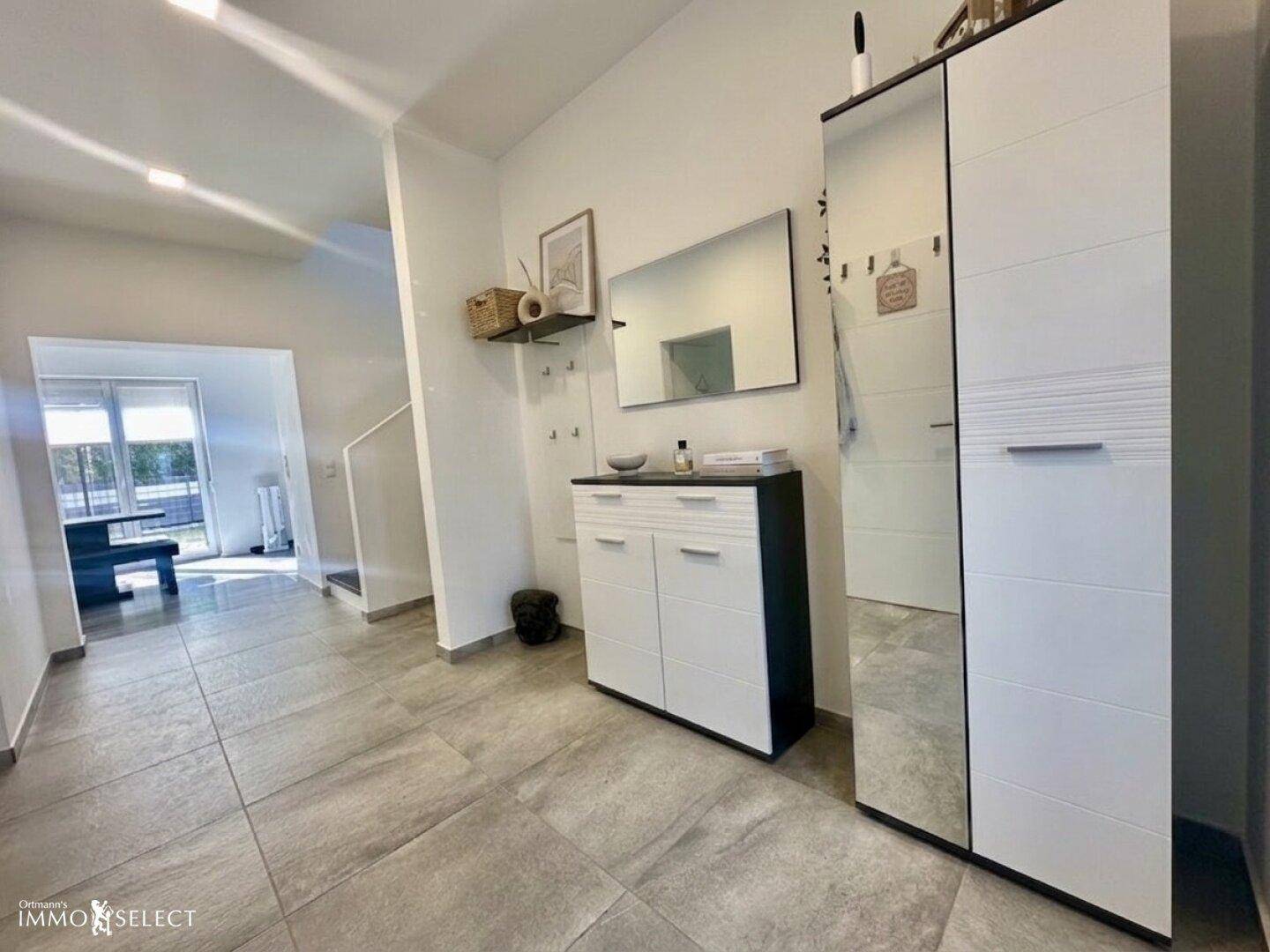 Eingangsbereich mit Fliesenboden, Spiegel und moderner Garderobe.