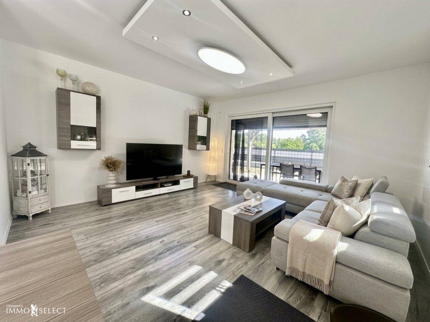 Geräumiges Wohnzimmer mit großem Sofa, Fernseher und Zugang zur Terrasse.