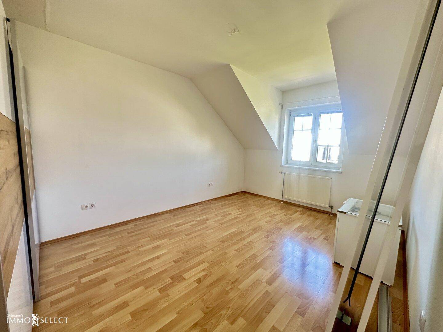 Dachgeschosszimmer mit Laminatboden und Fenster, ideal als Schlaf- oder Arbeitszimmer.