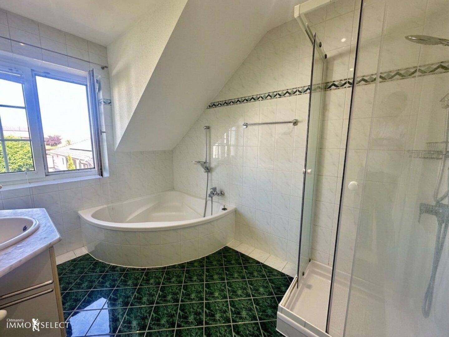 Badezimmer im Dachgeschoss mit Eckbadewanne, Duschkabine und Fenster.