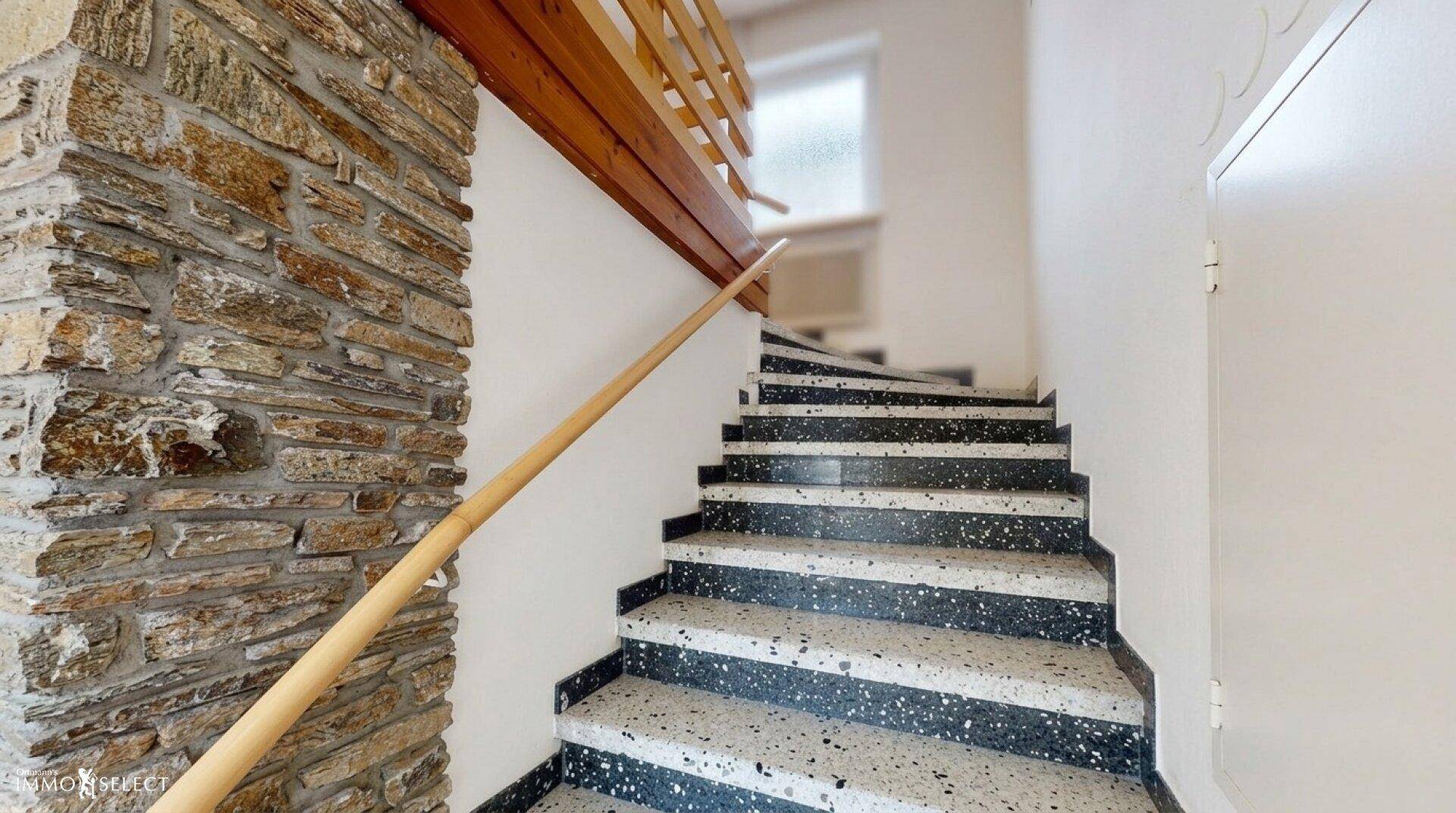 Treppenhaus mit Terrazzo-Stufen, Holzgeländer und dekorativer Steinwandverkleidung.