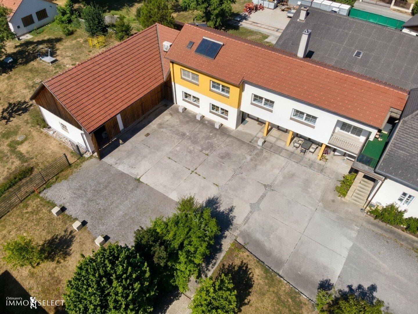 Luftaufnahme des Gebäudekomplexes mit großem Vorplatz und angrenzendem Nebengebäude.
