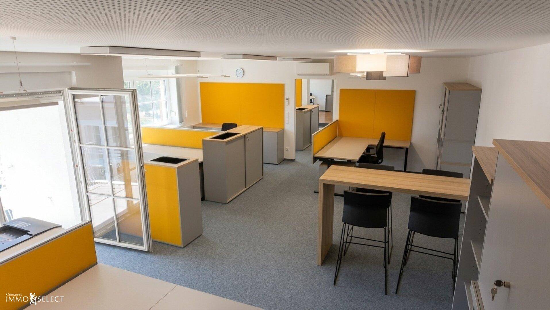 Großzügiges Büro mit mehreren Arbeitsbereichen, gelben Trennwänden und viel Tageslicht.