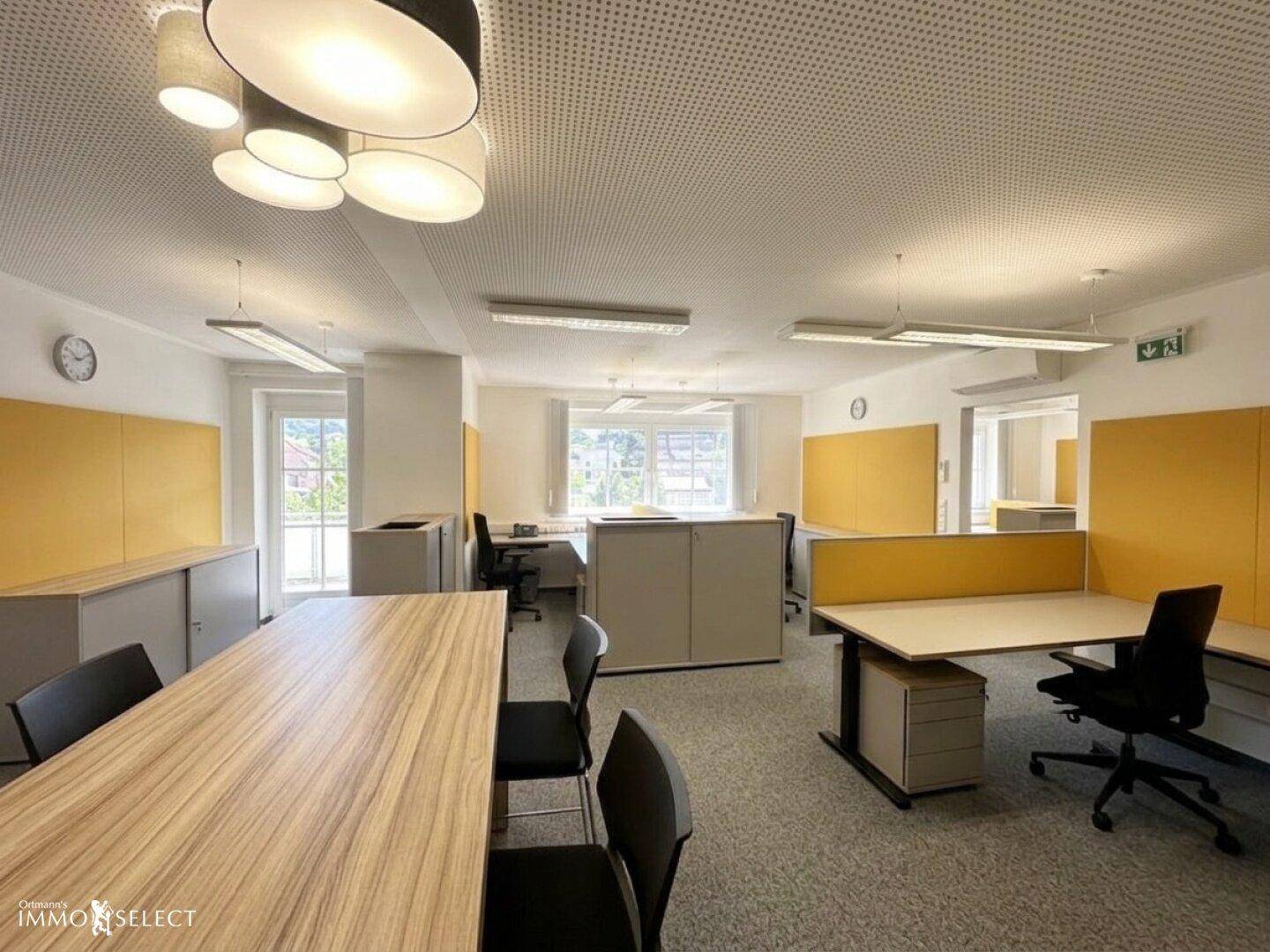 Modernes Großraumbüro mit ergonomischen Arbeitsplätzen, gelben Trennwänden und abgehängter Decke.
