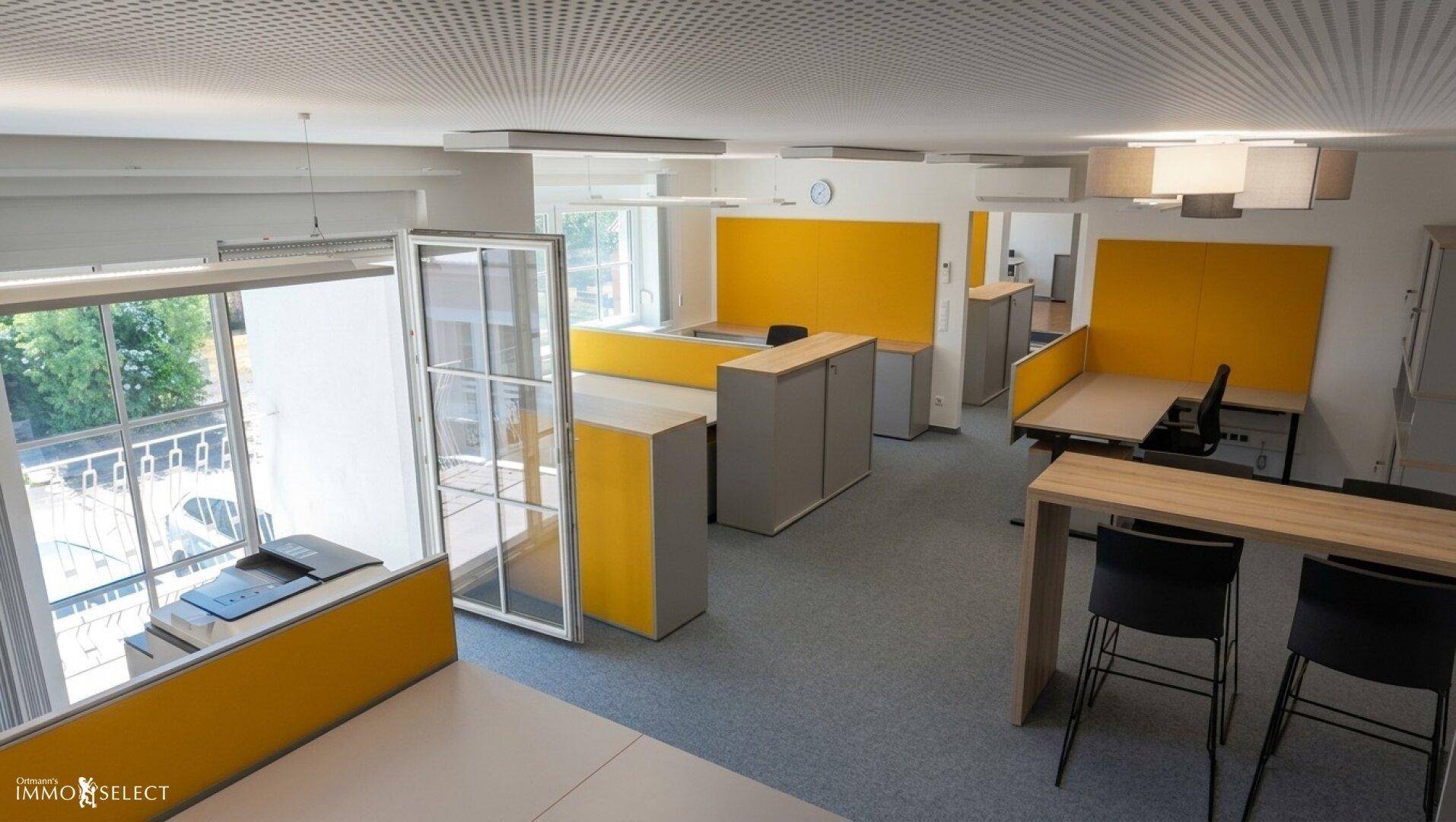 Offenes Büro mit modernen Möbeln, gelben Akzenten und Blick ins Grüne.