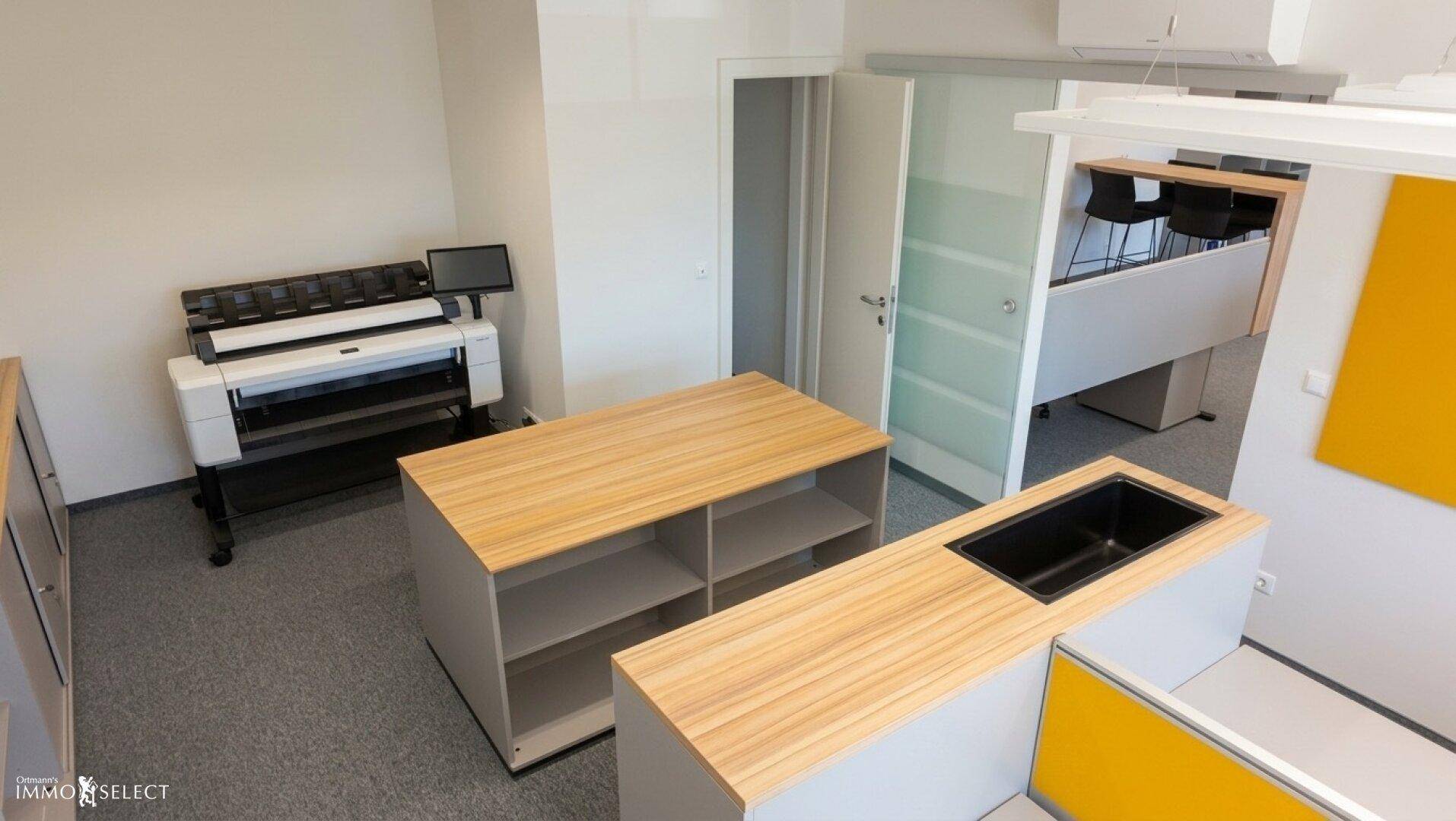 Bürobereich mit Druckerstation, Ablageflächen und einer kleinen Spüle.