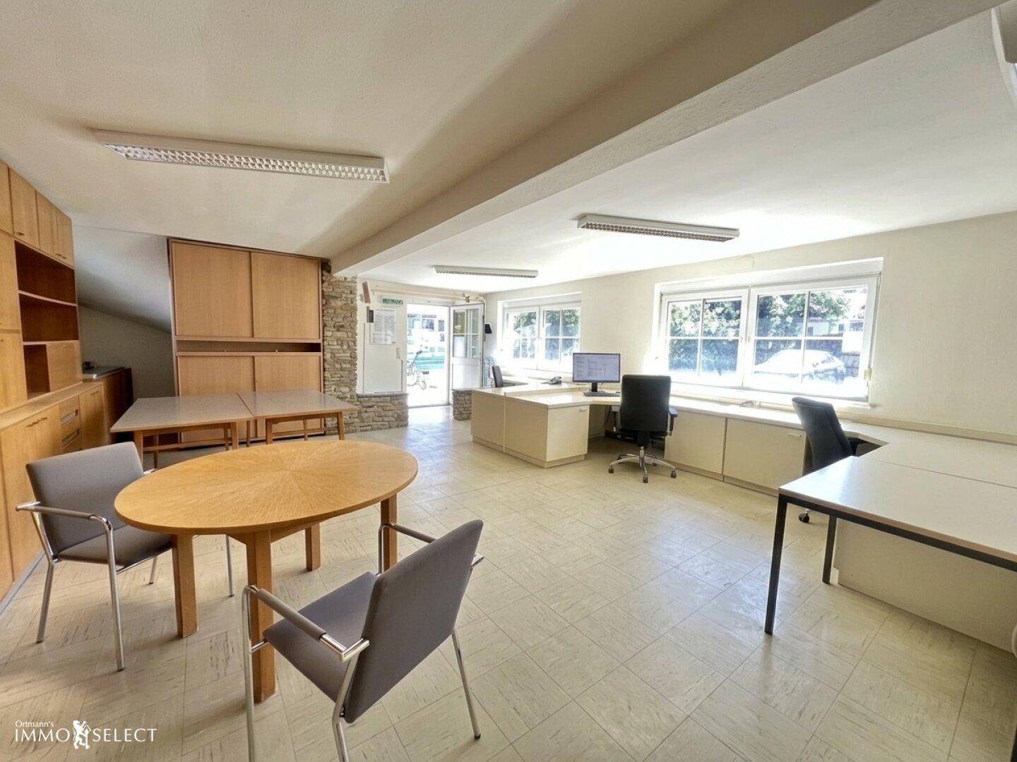 Großes Büro mit mehreren Arbeitsplätzen, Holzschränken und Blick ins Grüne.