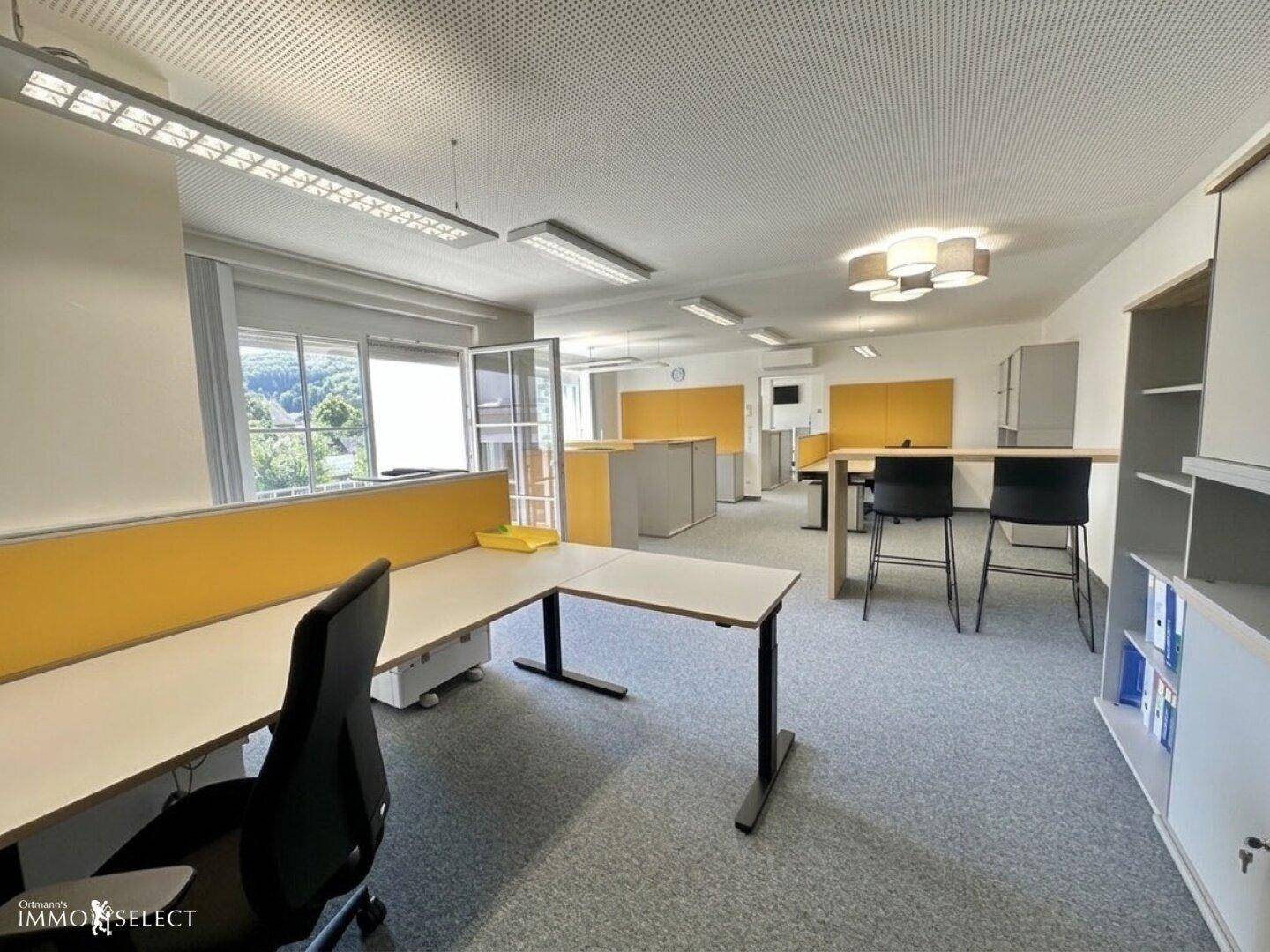 Modernes Großraumbüro mit ergonomischen Arbeitsplätzen, gelben Trennwänden und viel Tageslicht.