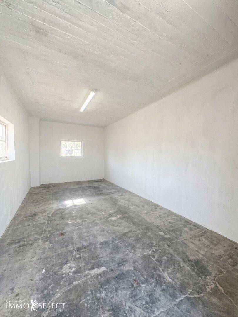 Leerer Raum mit Betonboden, weißen Wänden und kleinen Fenstern, ideal als Lager.