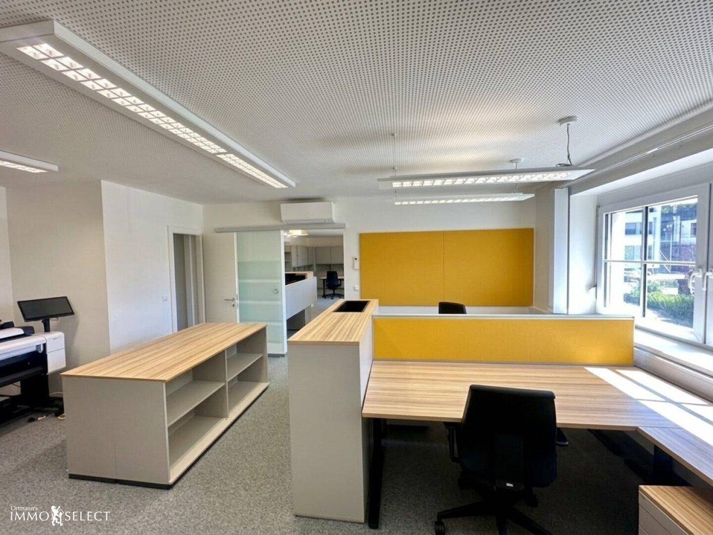 Helles und geräumiges Büro mit modernen Möbeln, Teppichboden und Klimaanlage.