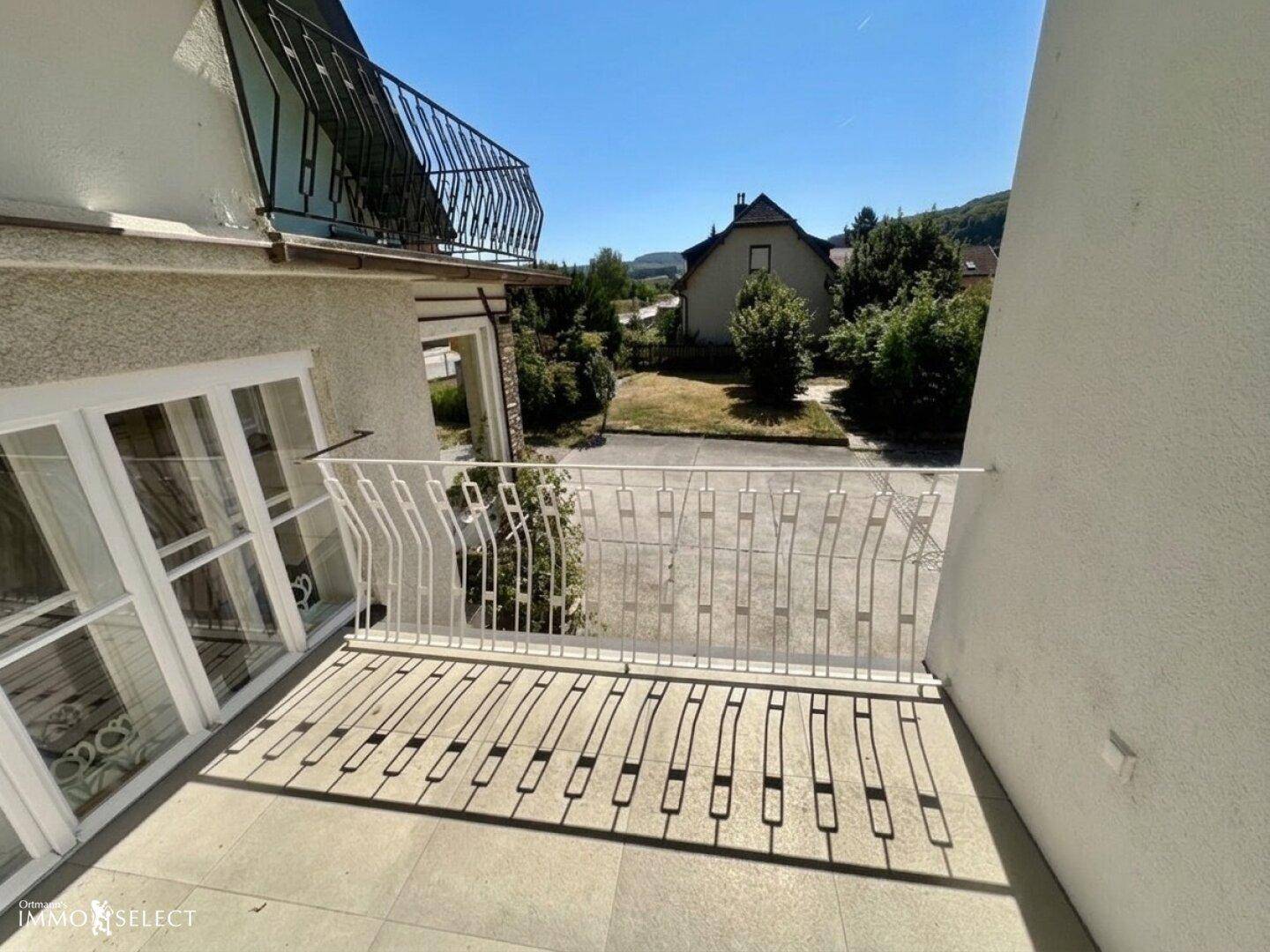 Sonniger Balkon mit weißem Geländer und Ausblick auf die umliegende Wohngegend und Natur.