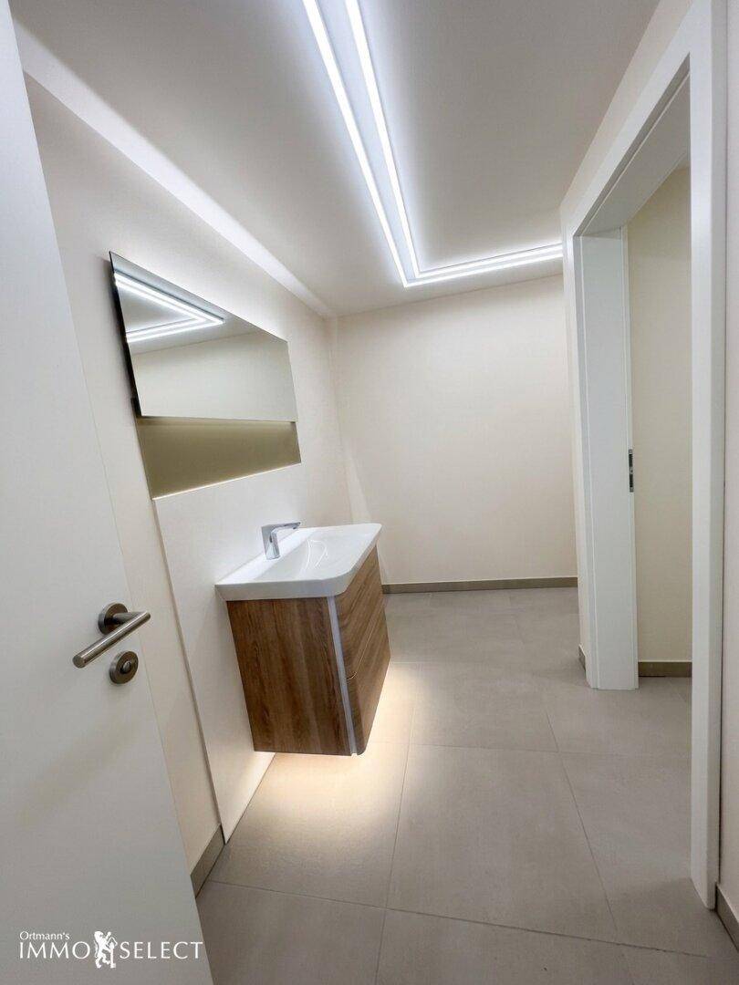 Modernes Badezimmer mit schwebendem Waschtisch, großem Spiegel und indirekter LED-Beleuchtung.