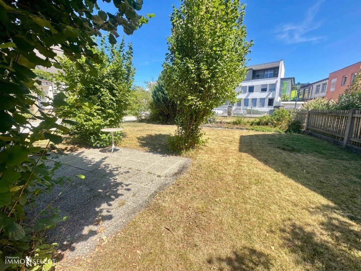 Gepflegter Gartenbereich mit Rasenfläche, kleiner Terrasse und Bäumen im Vordergrund.
