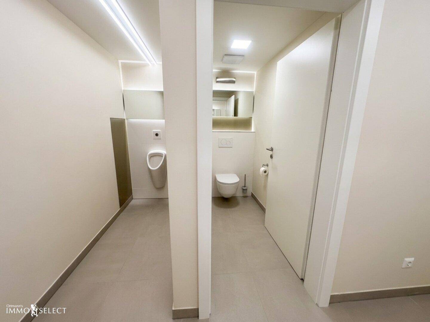 Moderne Toilettenanlage mit separaten Kabinen, wandhängendem WC und Urinal.