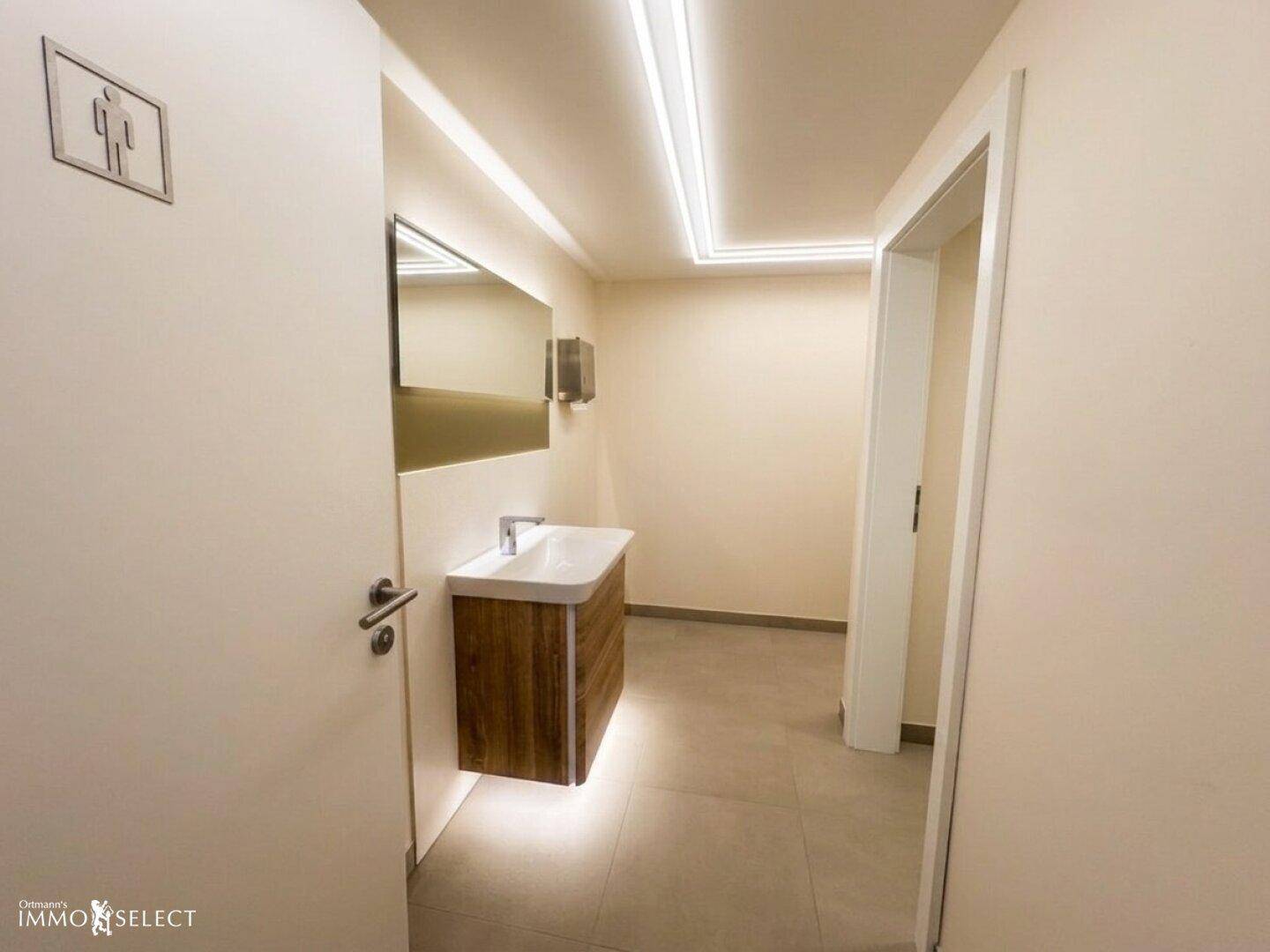 Modernes Badezimmer mit schwebendem Waschtisch, großem Spiegel und indirekter LED-Beleuchtung.