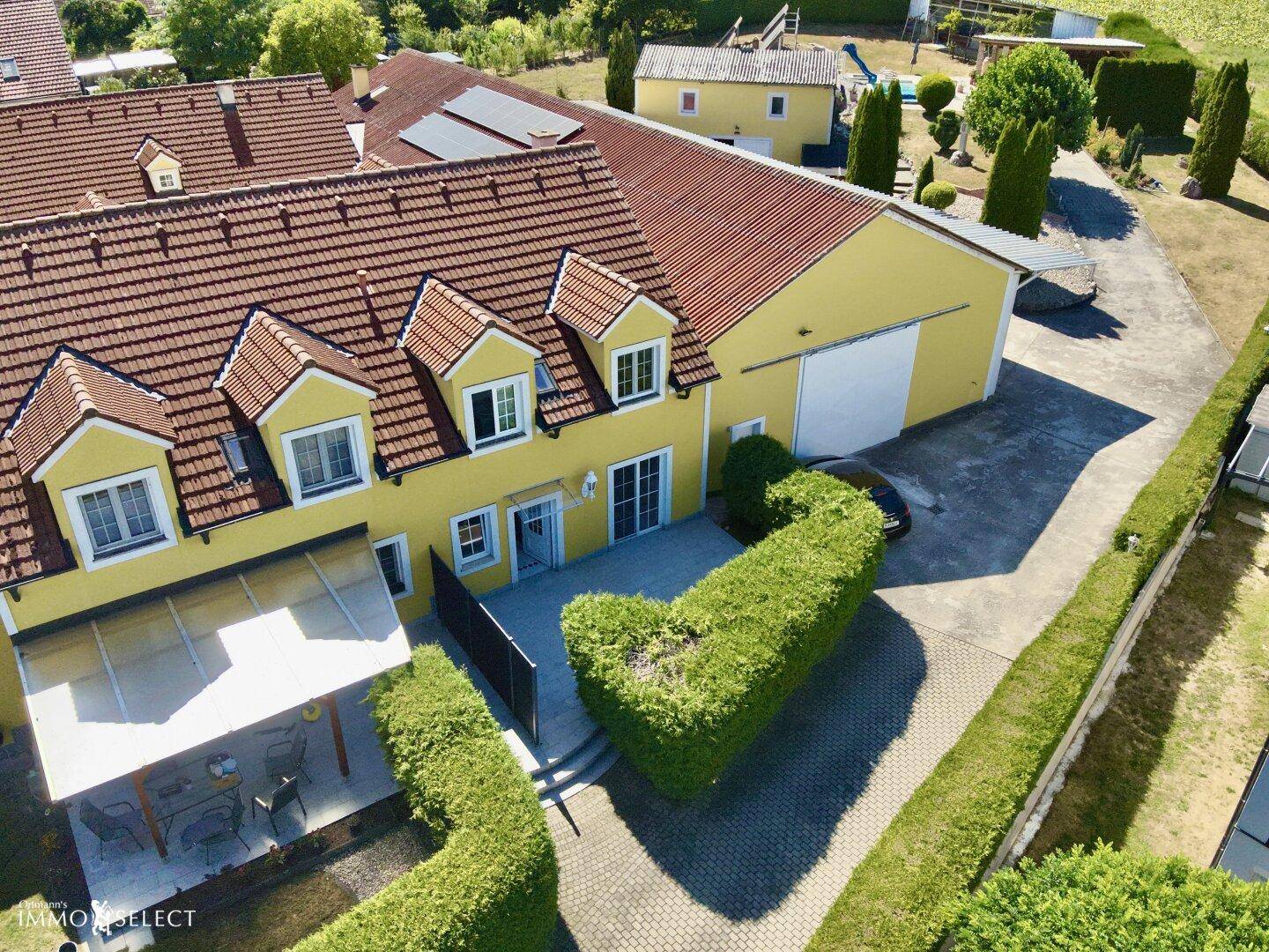 Luftaufnahme eines gepflegten Hauses mit gelber Fassade, rotem Ziegeldach und überdachter Terrasse.