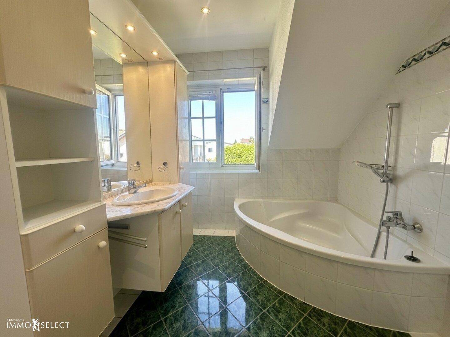 Badezimmer im Dachgeschoss mit Eckbadewanne, Einzelwaschbecken und Fenster.