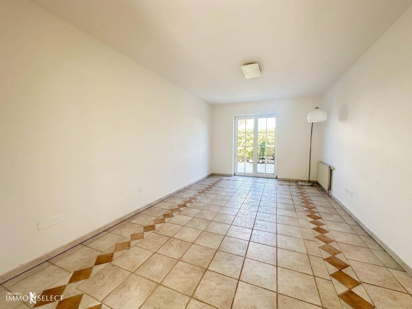 Geräumiger, unmöblierter Wohnbereich mit Fliesenboden und direktem Zugang zum Garten.
