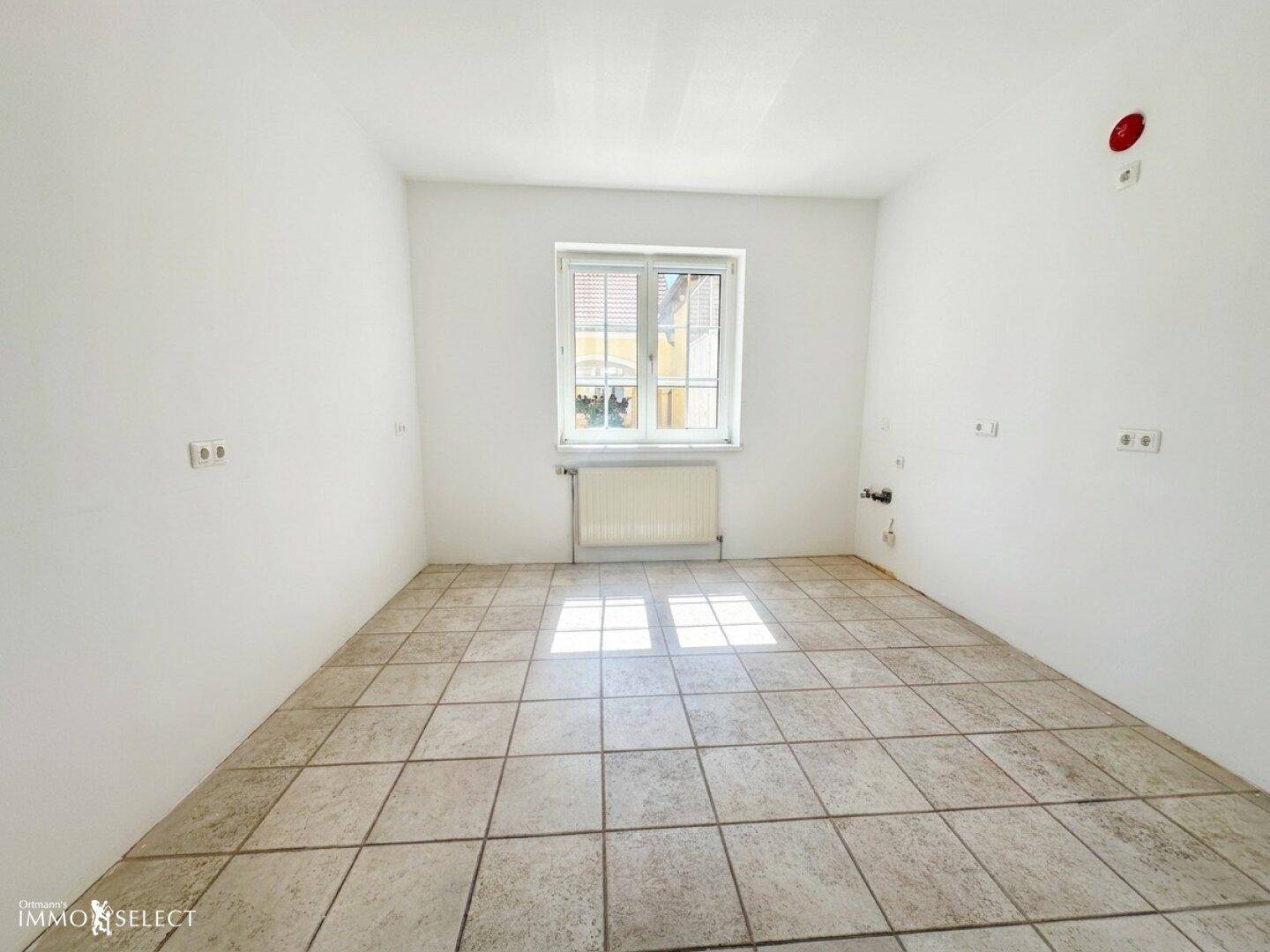 Leere Küche mit Fliesenboden und Fenster, bereit für die Installation von Geräten.