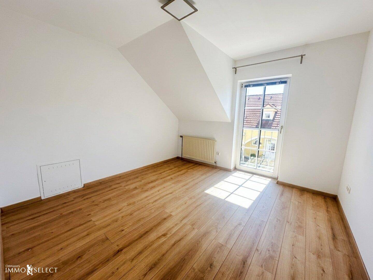 Helles Schlafzimmer im Dachgeschoss mit Laminatboden und französischem Balkon.
