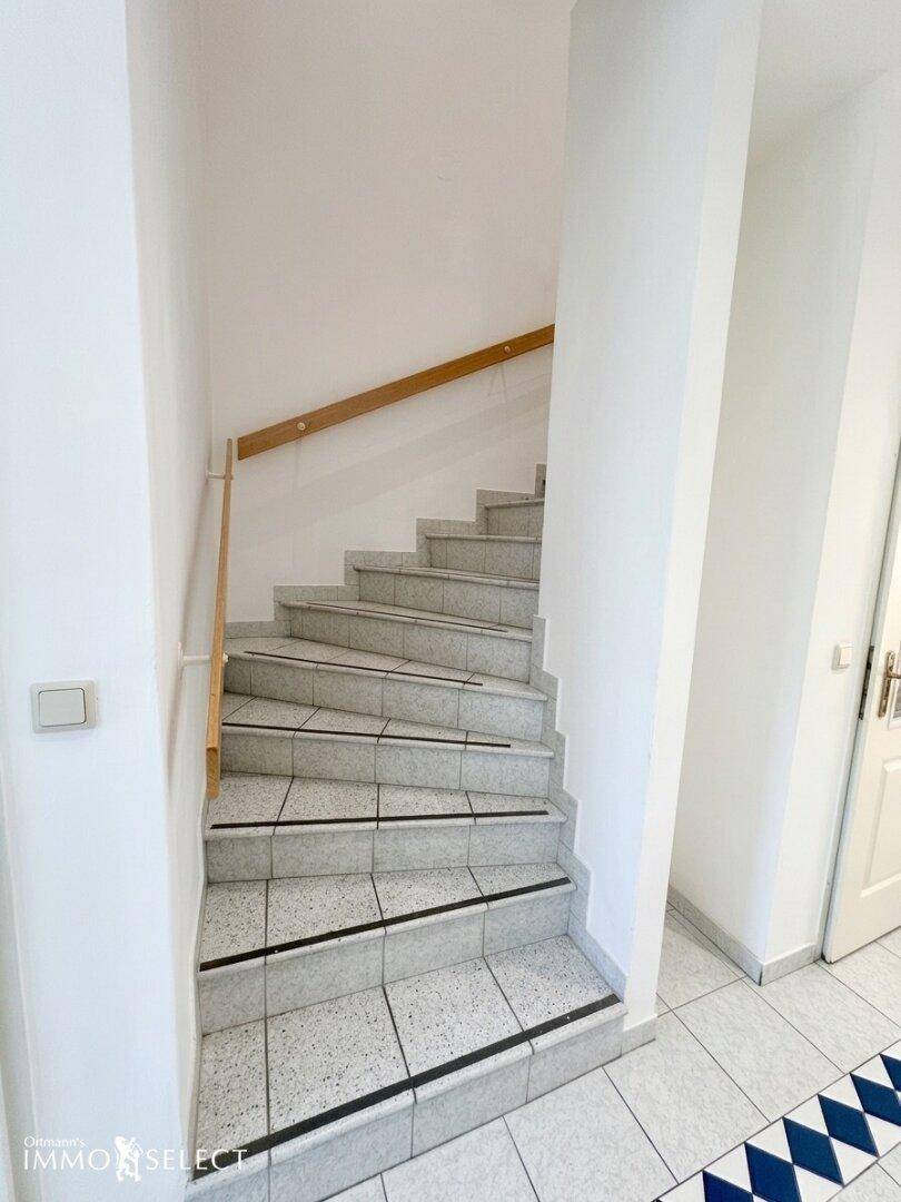 Treppenhaus mit gefliesten Stufen und Holzgeländer, das die Etagen verbindet.