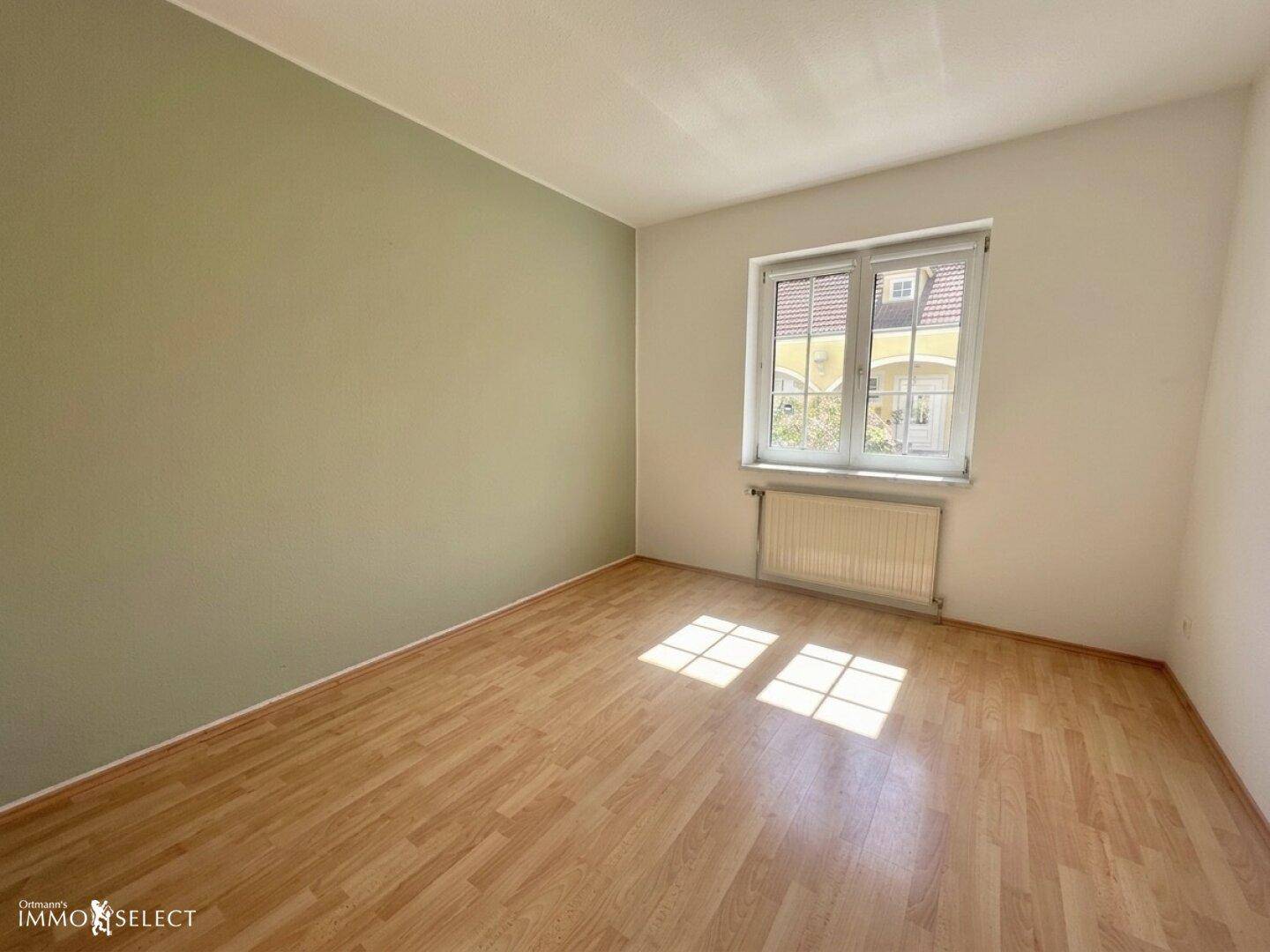 Schlafzimmer mit Laminatboden, einer grünen Akzentwand und viel Tageslicht.