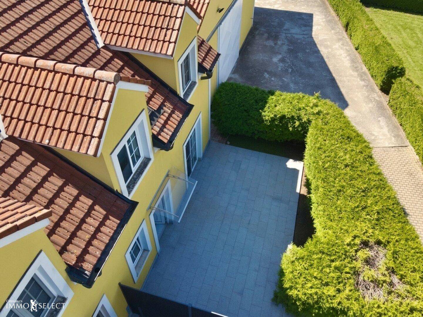 Luftaufnahme der gepflasterten Terrasse und des gepflegten Gartens am gelben Haus.