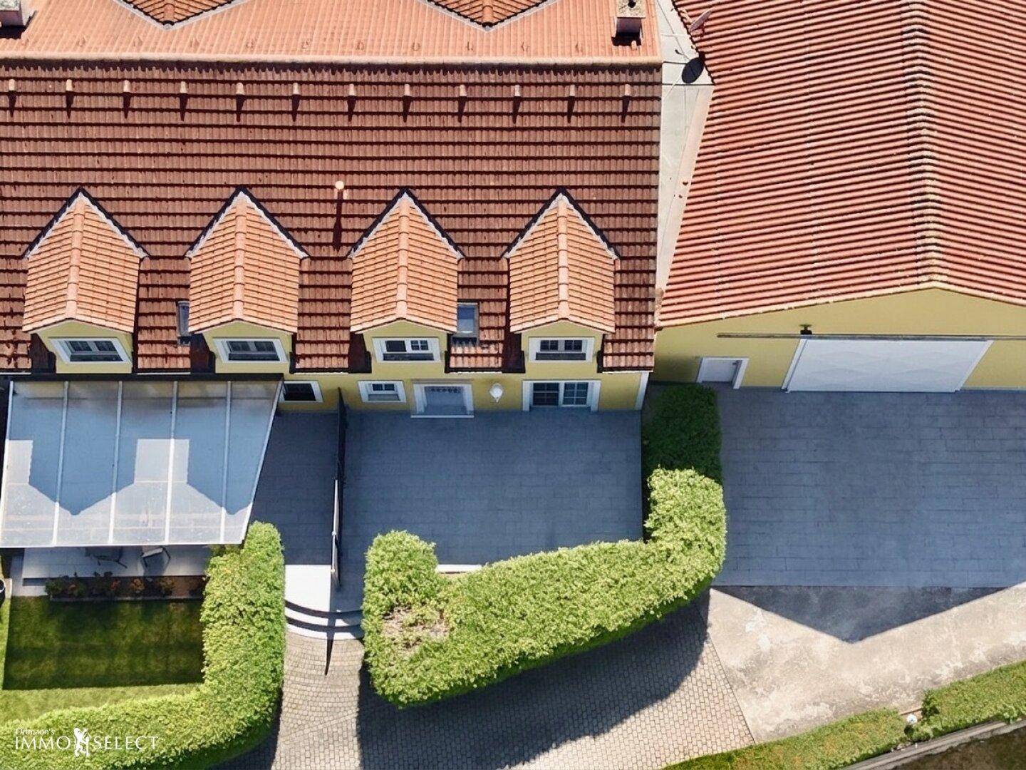 Draufsicht auf das gelbe Haus mit rotem Ziegeldach, Terrasse und Carport.